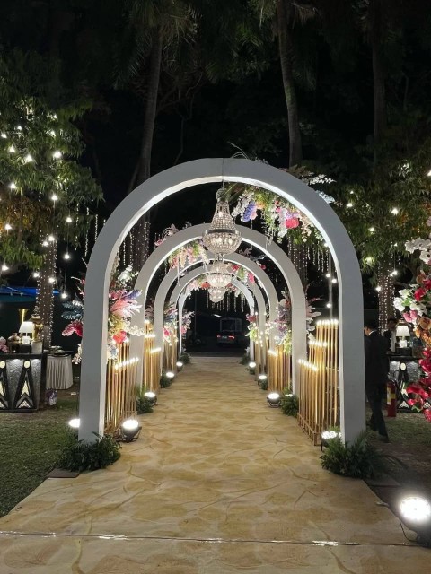 Elegant Punjabi wedding stage decoration with artificial flowers, gold accents, decorative panels, and chandelier lighting.