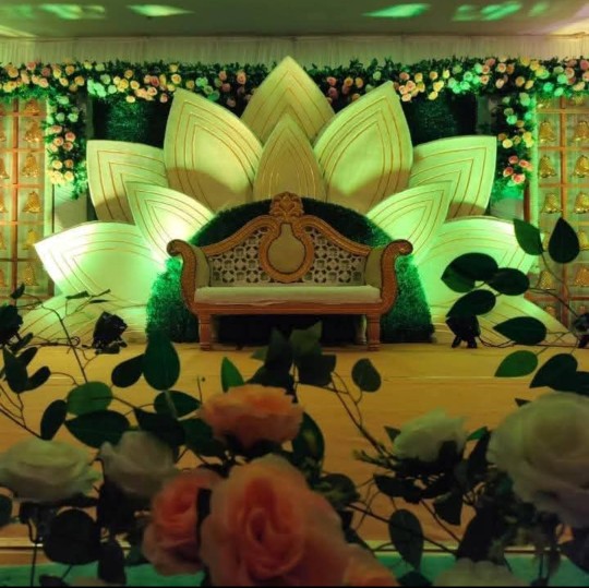 Gujarati wedding decoration with artificial flowers, golden decorative stands, and warm event lighting.